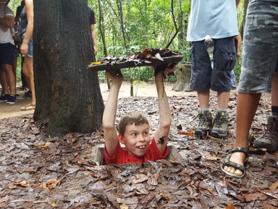 Bezoek aan de Cu Chi-tunnels in Vietnam, met een jongen die uit een tunnelopening omhoogkomt.
