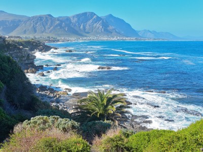 Kustlijn van de Tuinroute bij Hermanus met golven, rotsen en bergen op de achtergrond.