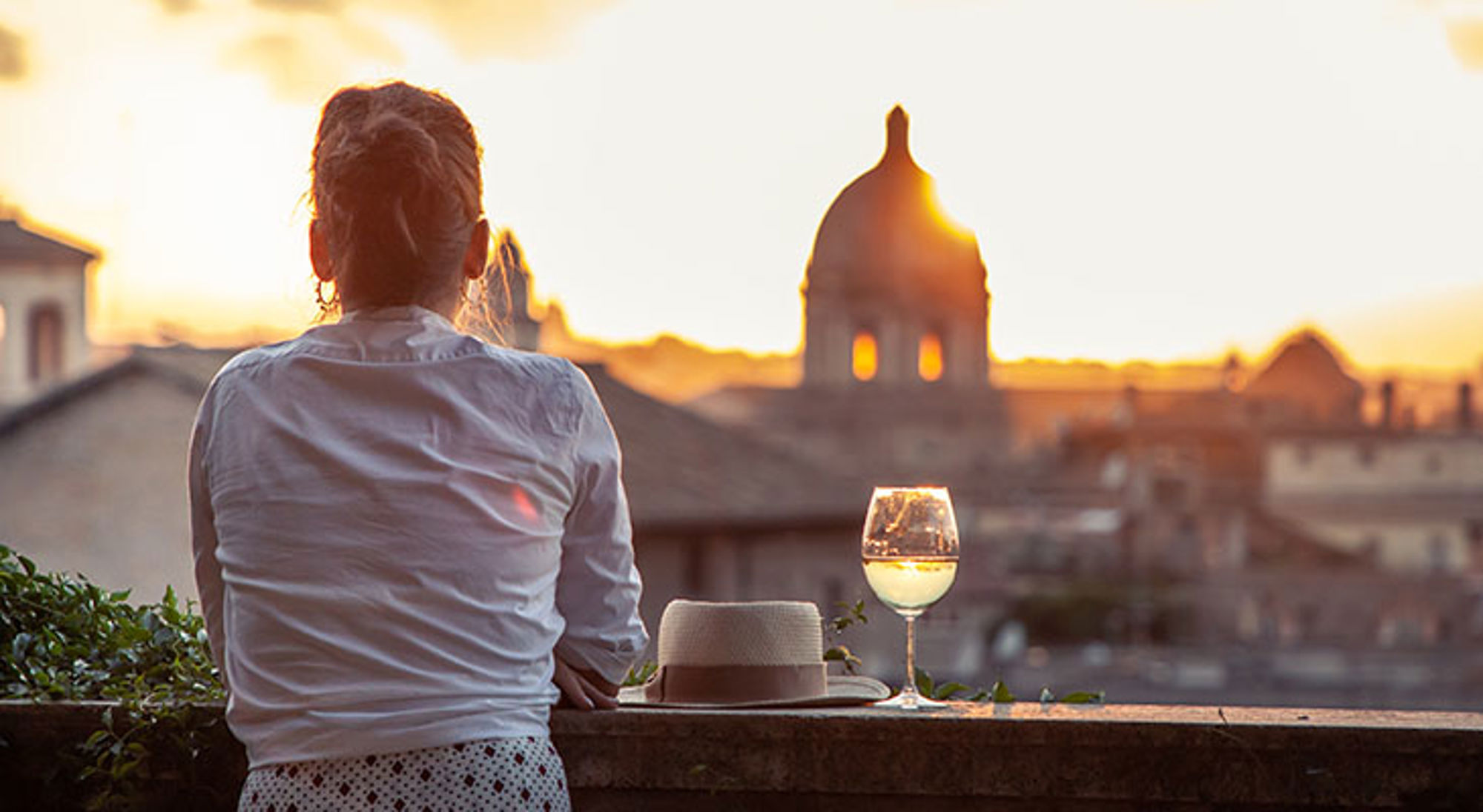 Il dolce far niente Vrouw geniet van een glas wijn bij zonsondergang met uitzicht op een historische stad en koepel.