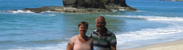 Carin en Theo op het strand in Costa Rica, met golven en een rotsachtig eiland op de achtergrond.