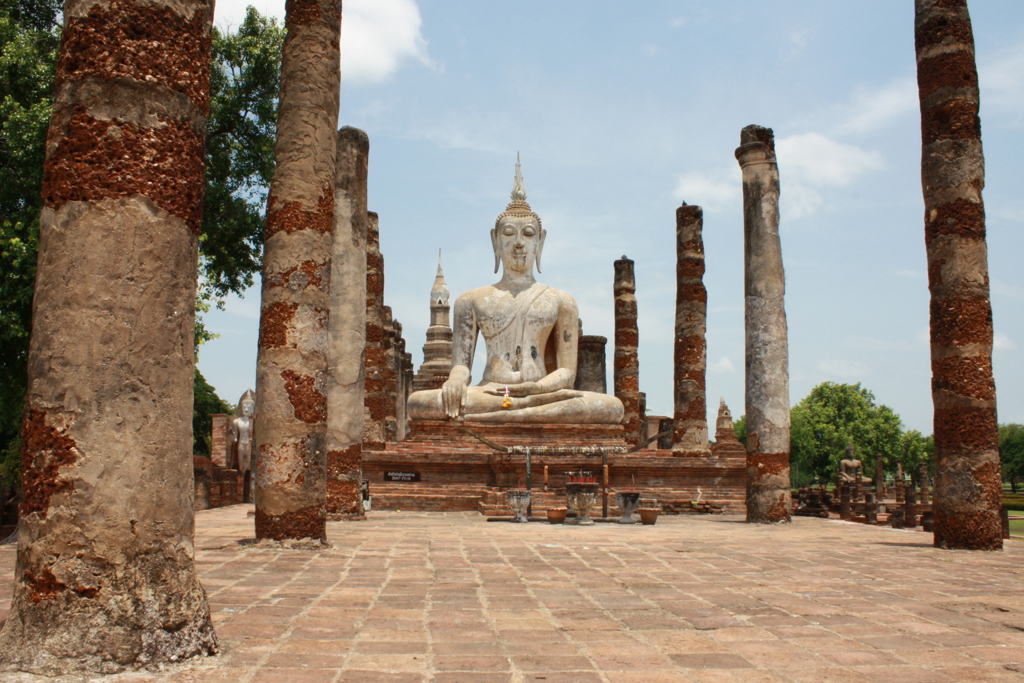 Grote zittende Boeddha tussen oude zuilen in het tempelcomplex van Sukhothai, Thailand.