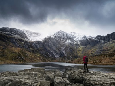 Wandelaar bij bergmeer met besneeuwde toppen in Snowdonia, Wales, tijdens de route Verenigd Koninkrijk & Ierland.