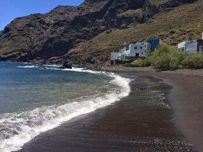 Zwart zandstrand aan de kust van Tenerife met golven, kliffen en een klein dorpje met witte huizen.