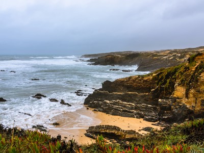 Rotsachtige kust met zandstrand en golven langs de Costa Vicentina in Alentejo en Algarve.