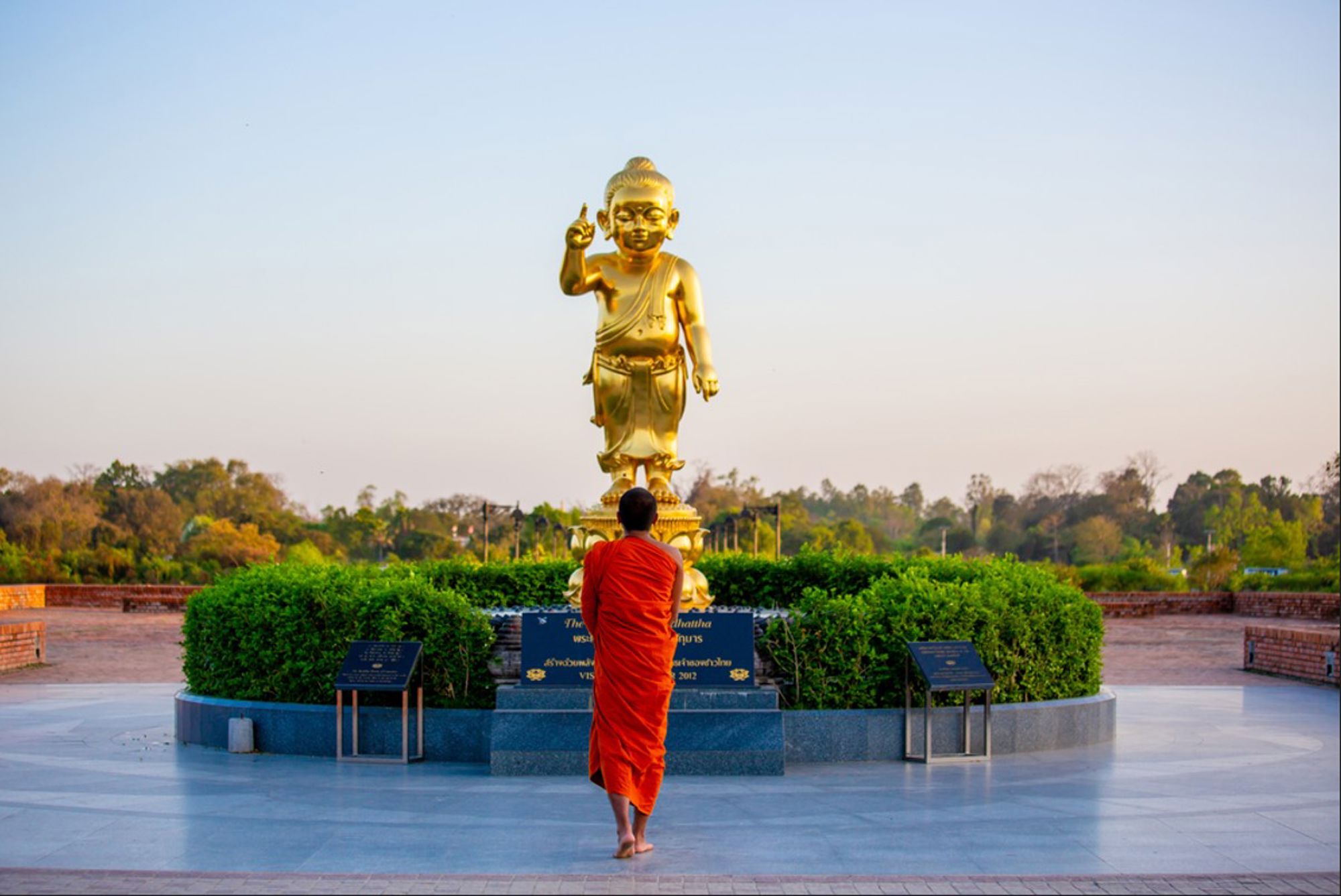 Monnik in oranje gewaad bij gouden Boeddhabeeld in Lumbini, Nepal.