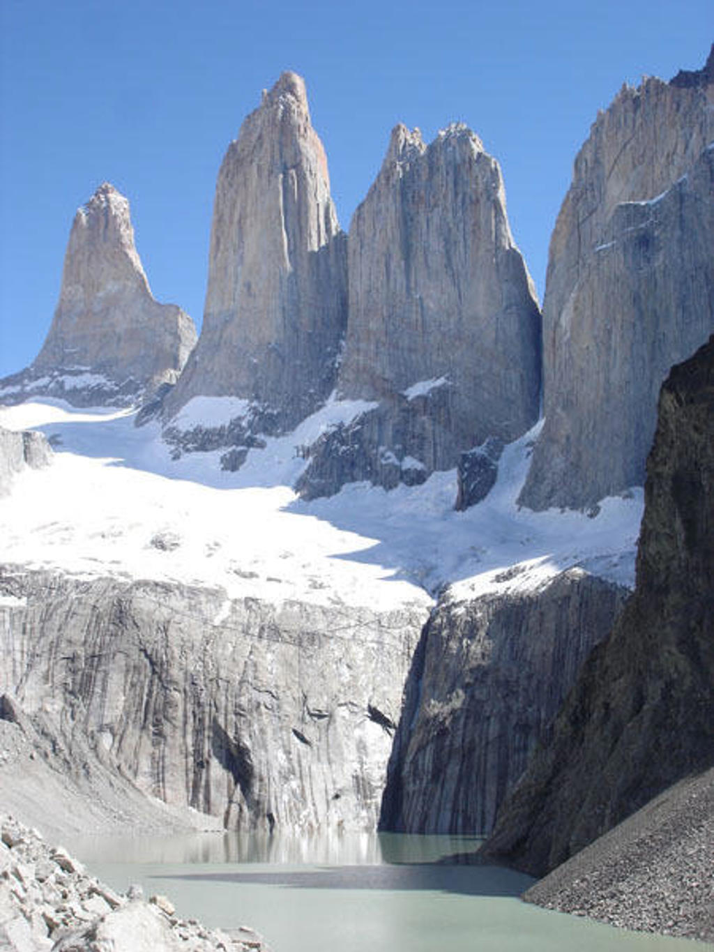 Besneeuwde bergtoppen en steile granieten pieken boven een azuurblauw meer in Patagonië.