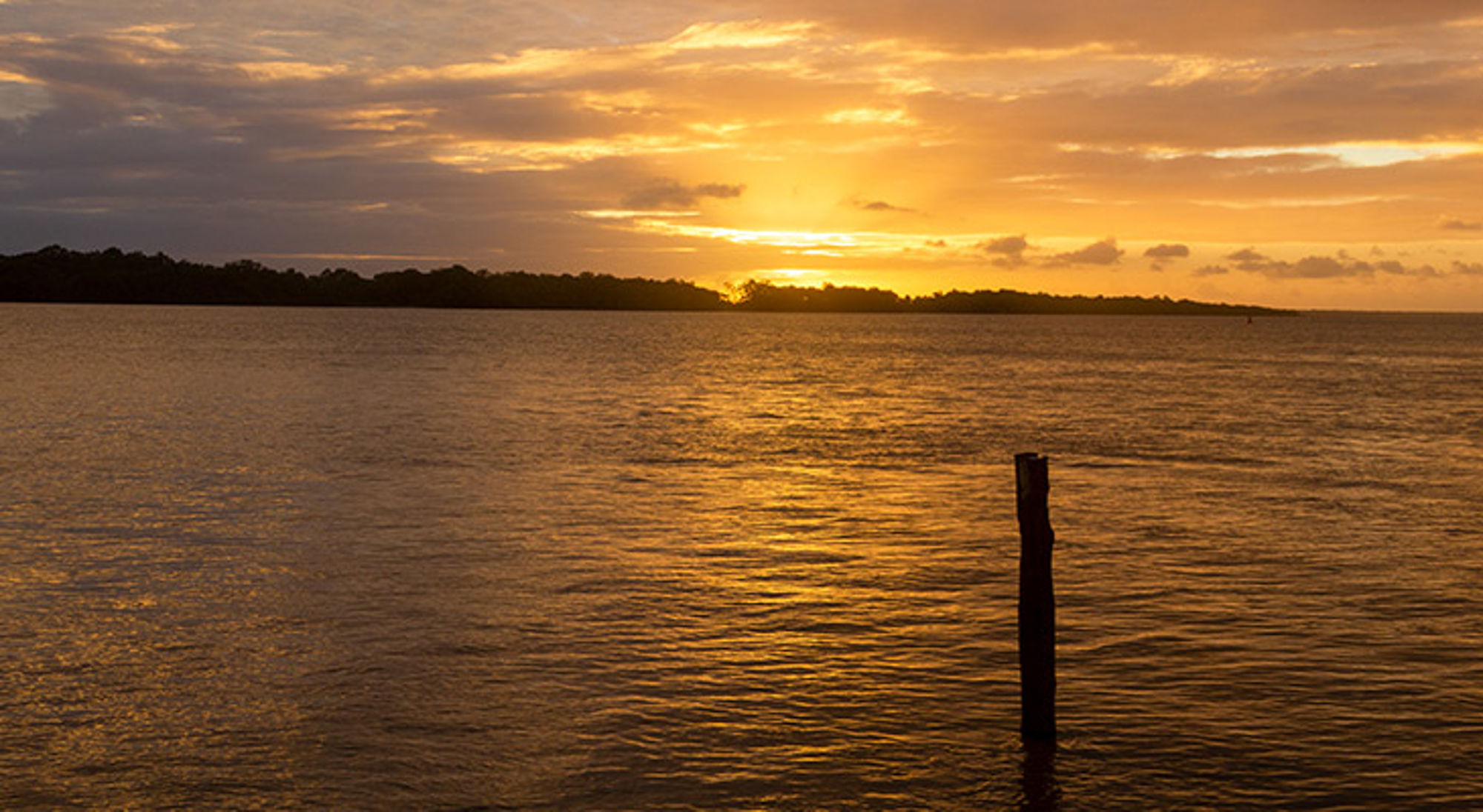 Zonsondergang boven een rustige zee met silhouet van een eiland aan de horizon.