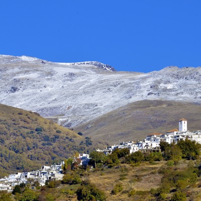 Wit bergdorp in de Alpujarras met besneeuwde Sierra Nevada op de achtergrond, Andalusië.