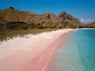 Roze zandstrand met helderblauw water en heuvels op de achtergrond, Route Kleine Sunda Eilanden.