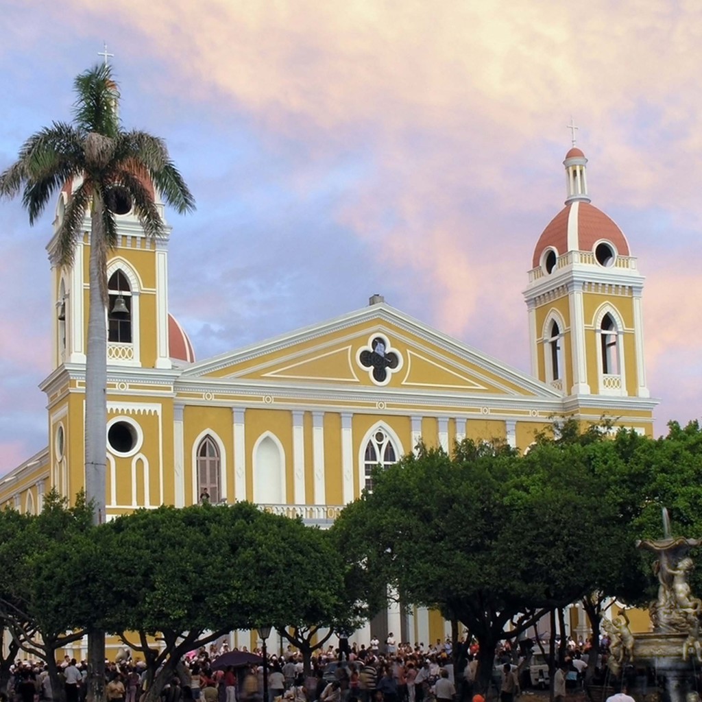 Gele kathedraal in Granada, Nicaragua, met palmbomen en plein bij zonsondergang.