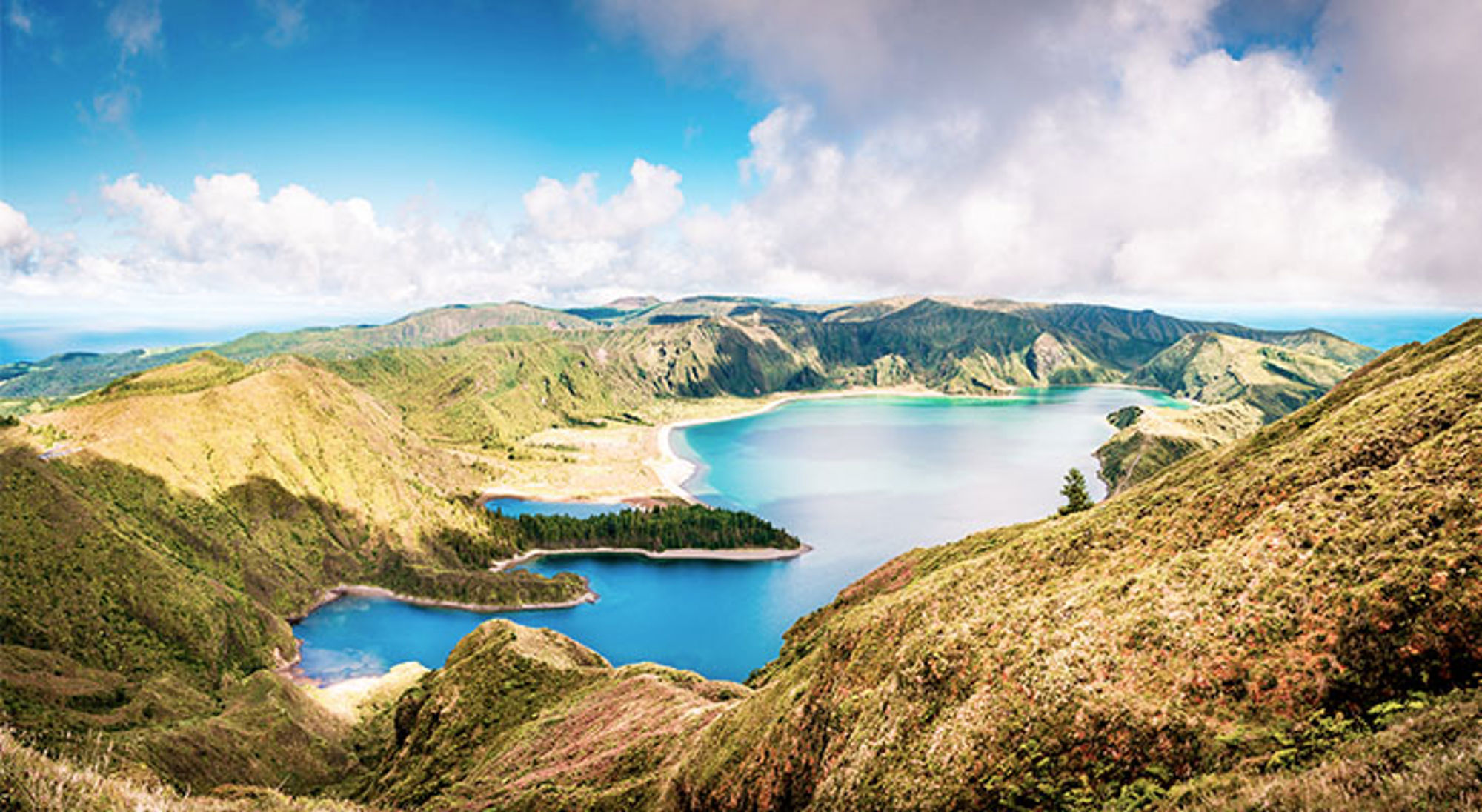 Panoramisch uitzicht op een kratermeer met turquoise water, groene heuvels en wolkenlucht.