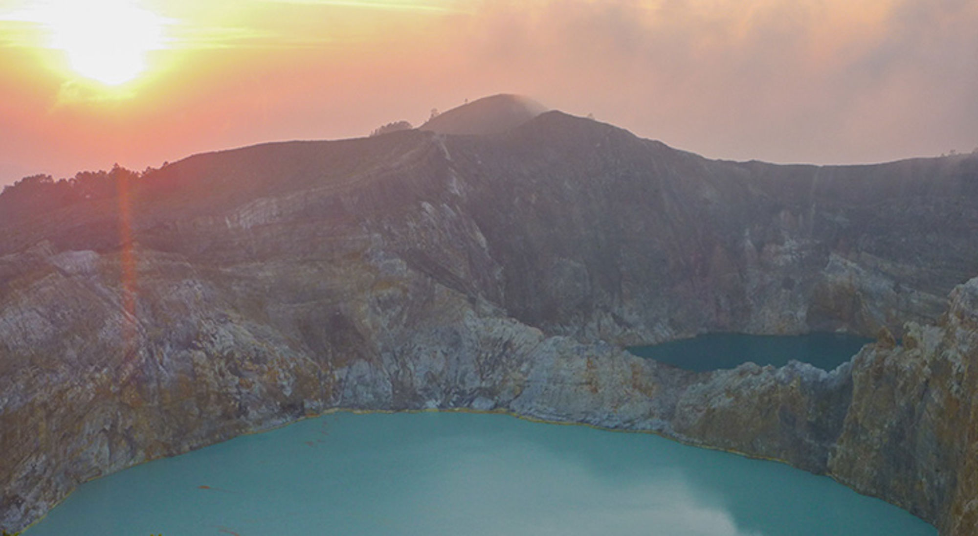 Kelimutu vulkaan, Flores, Indonesië Zonsopkomst boven een vulkaankrater met turkooizen kratermeer en rotsachtige bergwanden.