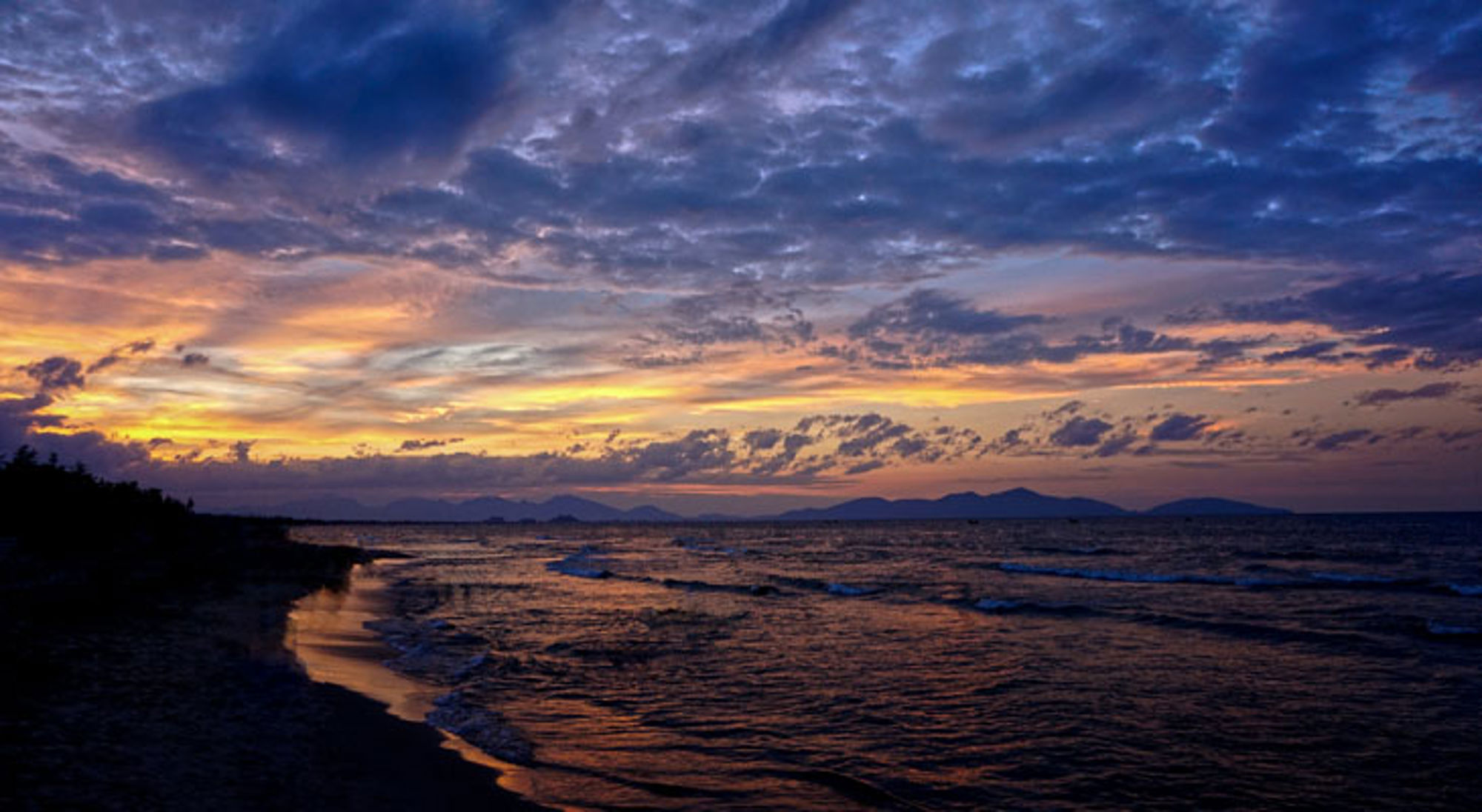 An Bang Beach Zonsondergang boven de kust in Vietnam, met golven op het strand en donkere wolken aan de horizon.