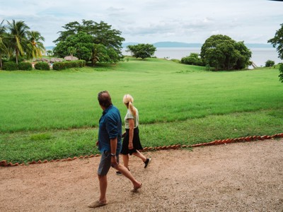Wandelaars op pad langs een groen grasveld met palmbomen en uitzicht op het water in Costa Rica.