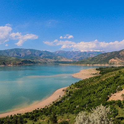 Panoramisch uitzicht op een bergmeer met groene heuvels en besneeuwde toppen in Oezbekistan.