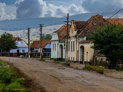 Landelijke dorpsstraat in Roemenië met kleurrijke huizen en bergen op de achtergrond.
