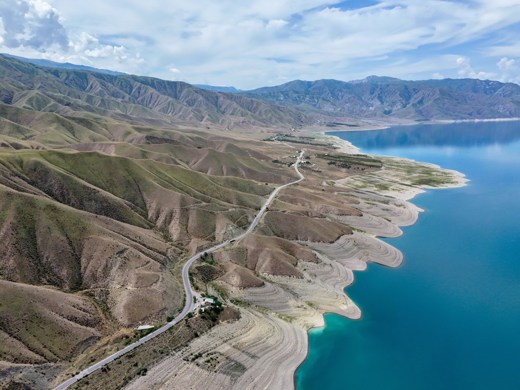 Panoramisch uitzicht op een bergweg langs een helderblauw meer in Kirgistan, tijdens wandelreis langs de Zijderoute.