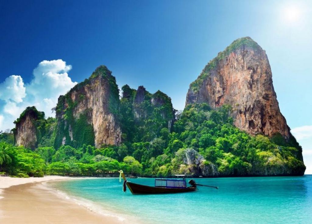Longtailboot bij een tropisch strand met kalkstenen kliffen en turquoise zee in Thailand.