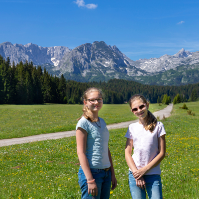 Twee meisjes in een bergweide met dennenbos en ruige bergen in Montenegro, tijdens familiereis Kroatië en Montenegro.