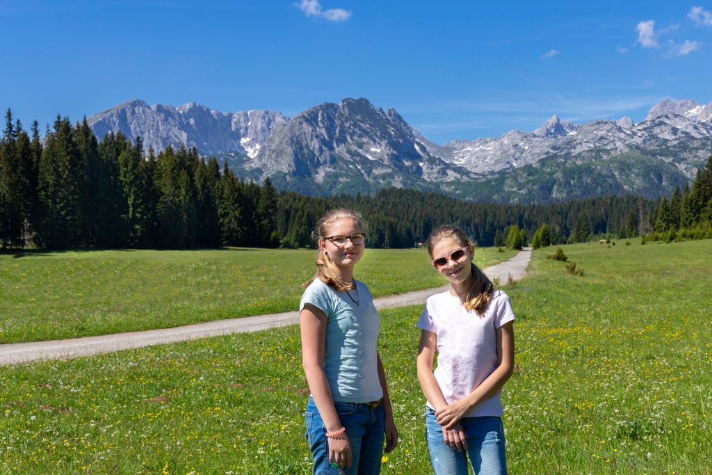 Twee meisjes in een bergweide met dennenbos en ruige bergen in Montenegro, tijdens familiereis Kroatië en Montenegro.