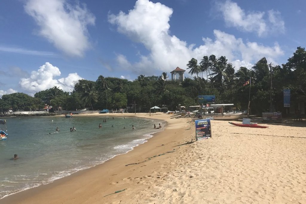 Zandstrand in Sri Lanka met zwemmers, palmbomen en vissersboten langs de kust.