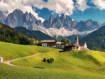 Groene alpenweide met kerk en boerderijen, met de Dolomieten op de achtergrond tijdens de Route Centraal Europa.