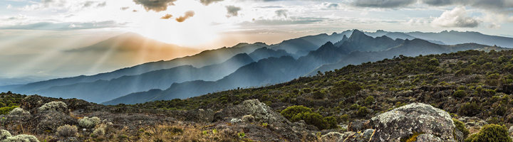Panoramisch uitzicht vanaf Mount Meru in Tanzania met rotsen, struikgewas en bergketens in de ochtendzon.