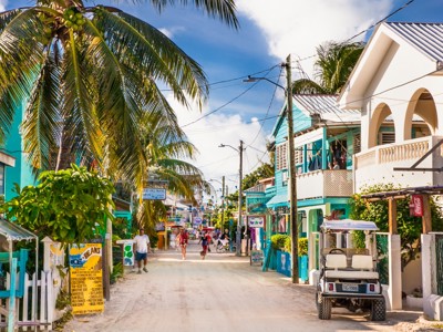 Straat in San Pedro, Belize met palmbomen, kleurrijke huizen en mensen op de zandweg.