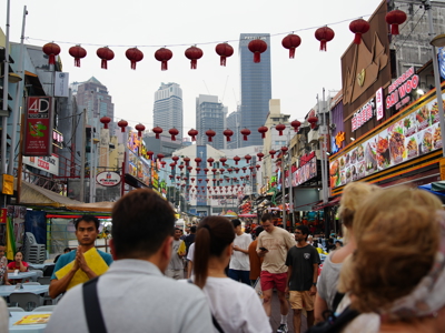 Drukke straatmarkt in Kuala Lumpur met rode lantaarns en skyline op de achtergrond.
