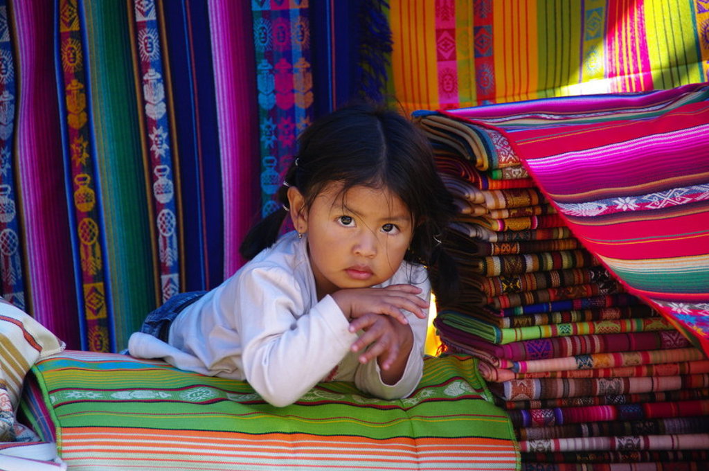 Meisje tussen kleurrijke geweven doeken op een markt in Ecuador, tijdens de groepsrondreis Ecuador Hoogtepunten.