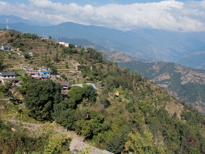 Terrasvelden en bergdorp op een groene helling met uitzicht op de Nepalese Himalaya tijdens Route Nepal.