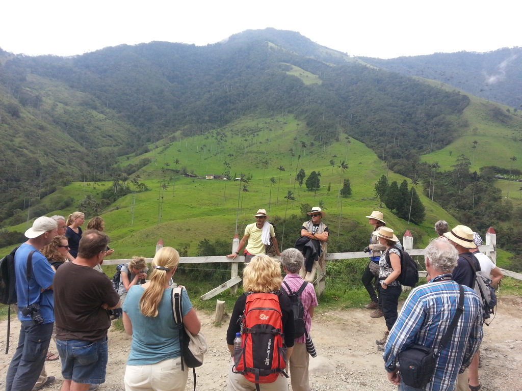 Groepsrondreis Colombia: reizigers luisteren naar een gids bij een uitzichtpunt met groene bergen op de achtergrond.