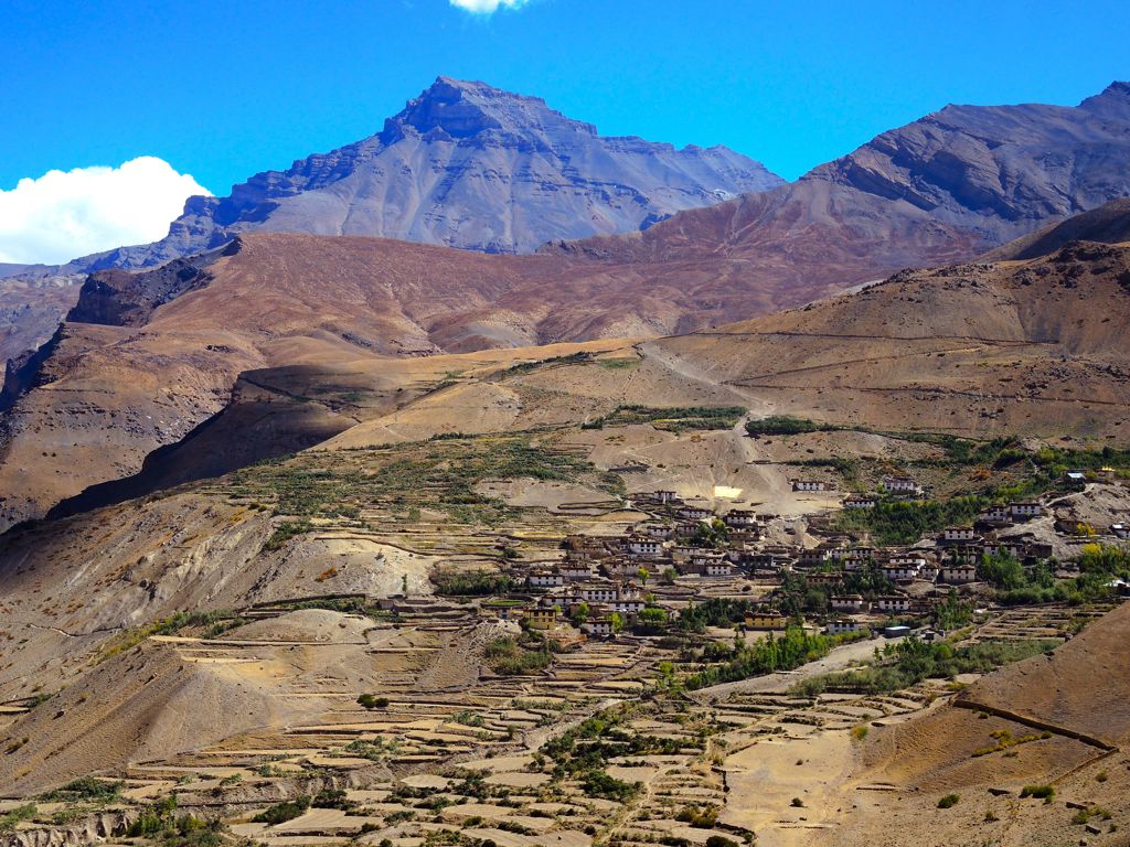 Bergdorp met terrassen en akkers in Ladakh, India, met hoge Himalayapieken op de achtergrond.