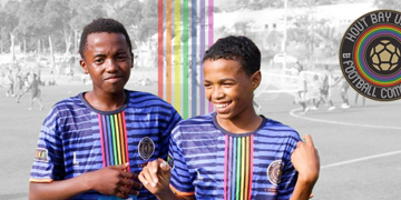 Twee jeugdspelers van Hout Bay United Football Community in clubshirt op het voetbalveld.