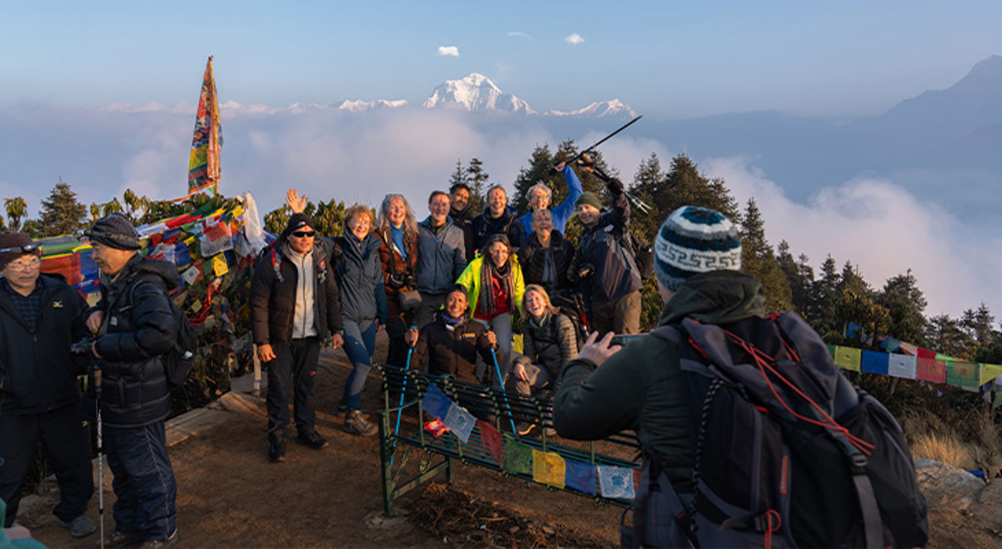Poon Hill Groep wandelaars poseert op een uitkijkpunt met gebedsvlaggen en besneeuwde bergtoppen op de achtergrond.