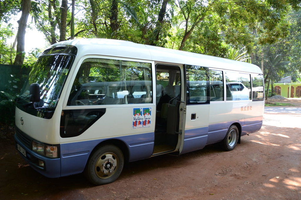 Witte minibus voor groepsrondreis Sri Lanka, geparkeerd langs een groene weg.