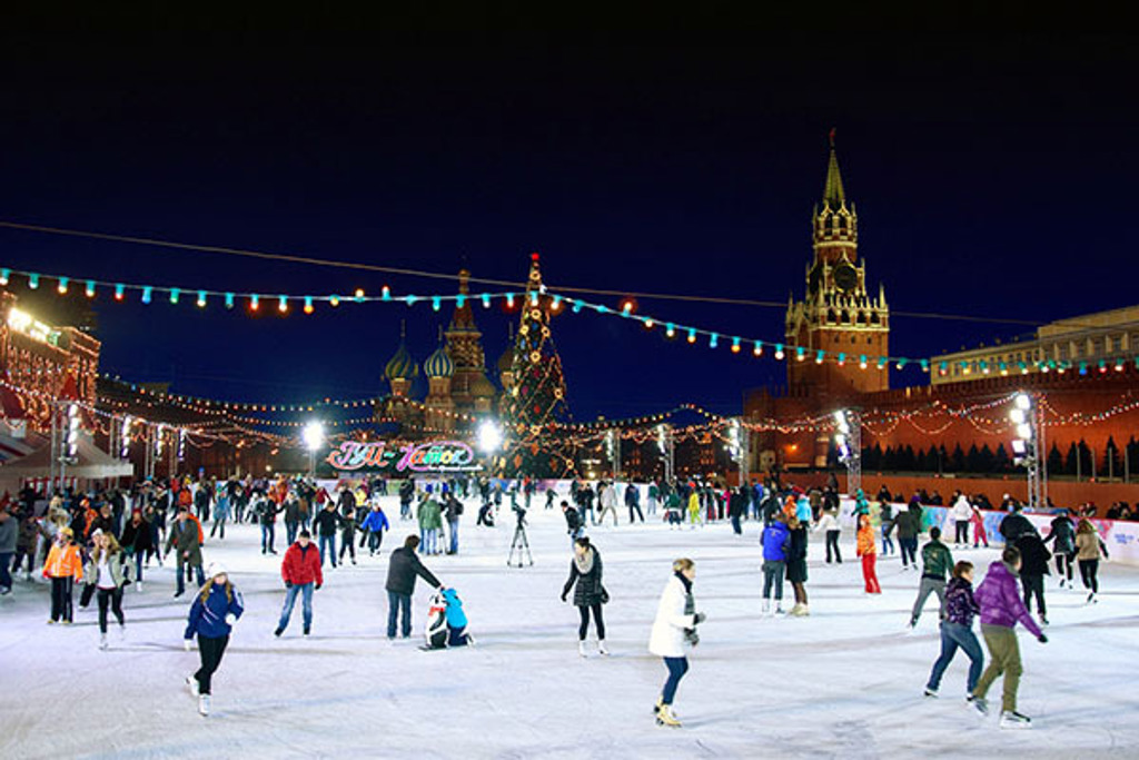 Schaatsers op de ijsbaan op het Rode Plein in Moskou, met kerstverlichting en het Kremlin in de winter.