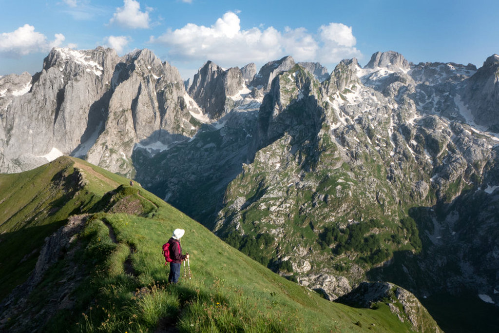 Wandelaar op bergkam met uitzicht op de Peaks of the Balkan, ruige rotsen en sneeuwvelden.