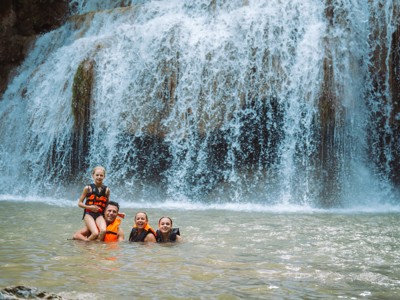 Gezin zwemt met zwemvesten bij een waterval tijdens de 21-daagse route door Thailand.