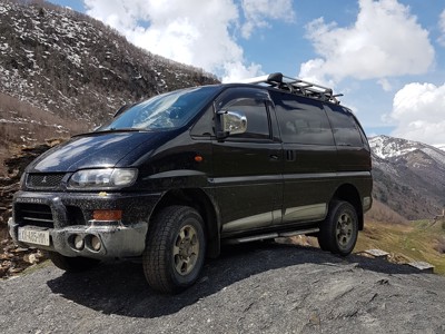 Zwarte 4x4-minibus op bergweg in Georgië, met besneeuwde bergen op de achtergrond.