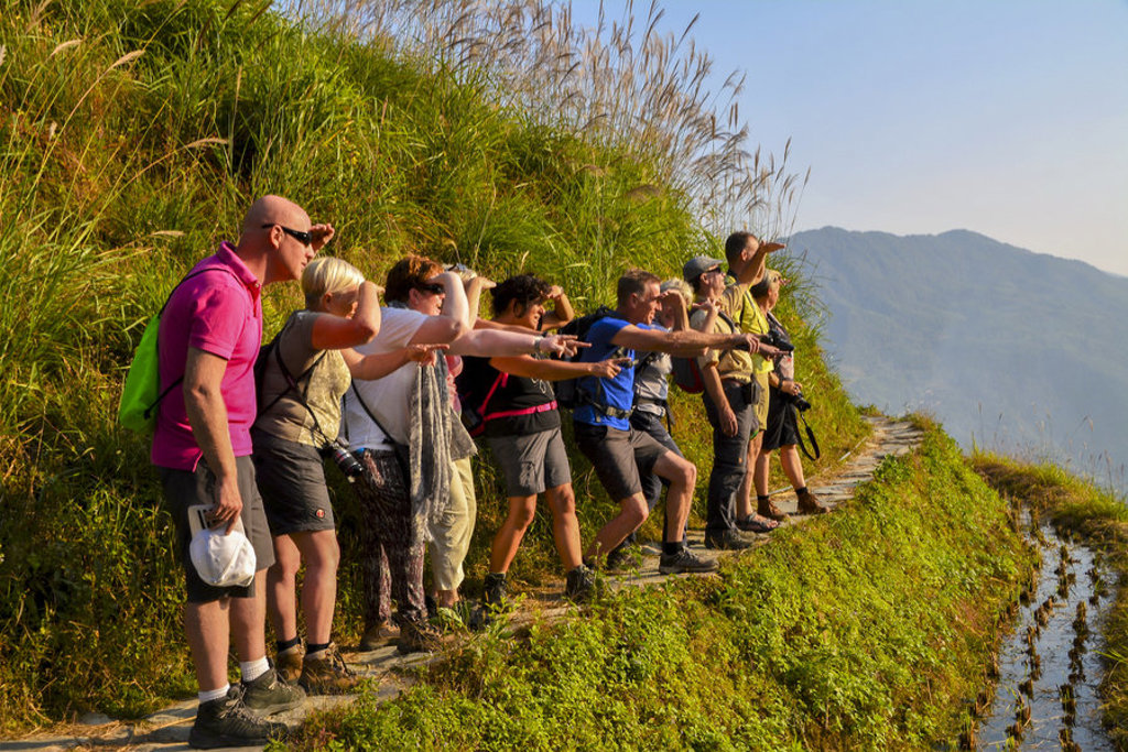 Groep reizigers tijdens groepsrondreis China Hoogtepunten bij rijstterrassen, wijzend naar het berglandschap.