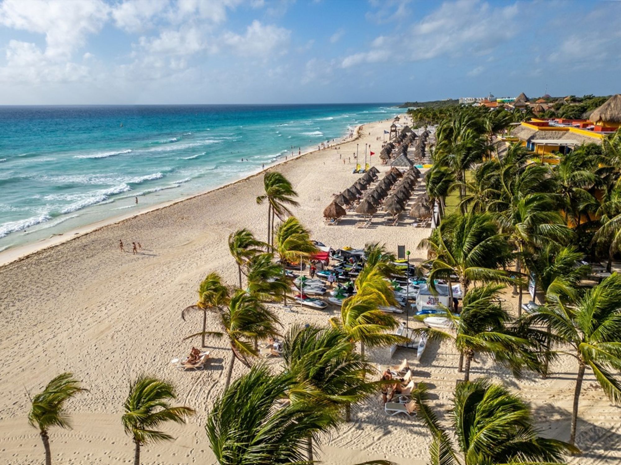 Zandstrand in Mexico met palmbomen, ligbedden en rieten parasols langs de turquoise zee.