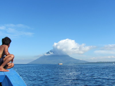 Man op boeg van boot met uitzicht op vulkaan op de Bangka-eilanden tijdens Route Sulawesi.