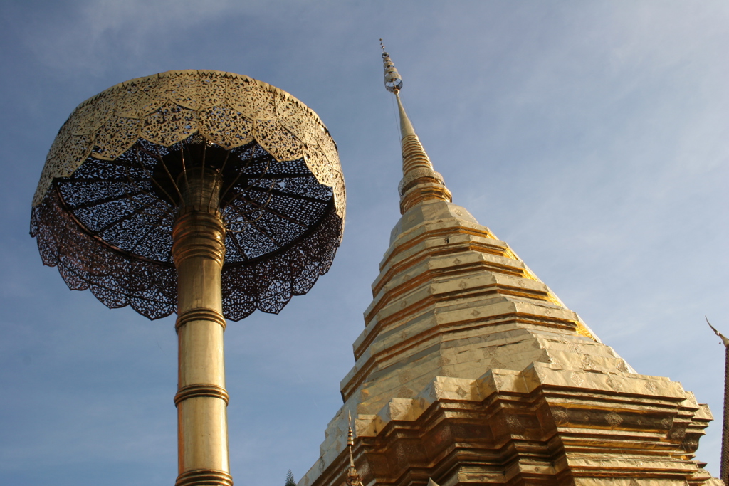 Gouden boeddhistische tempelstupa met sierlijke parasol, hoog tegen de blauwe lucht in Thailand.