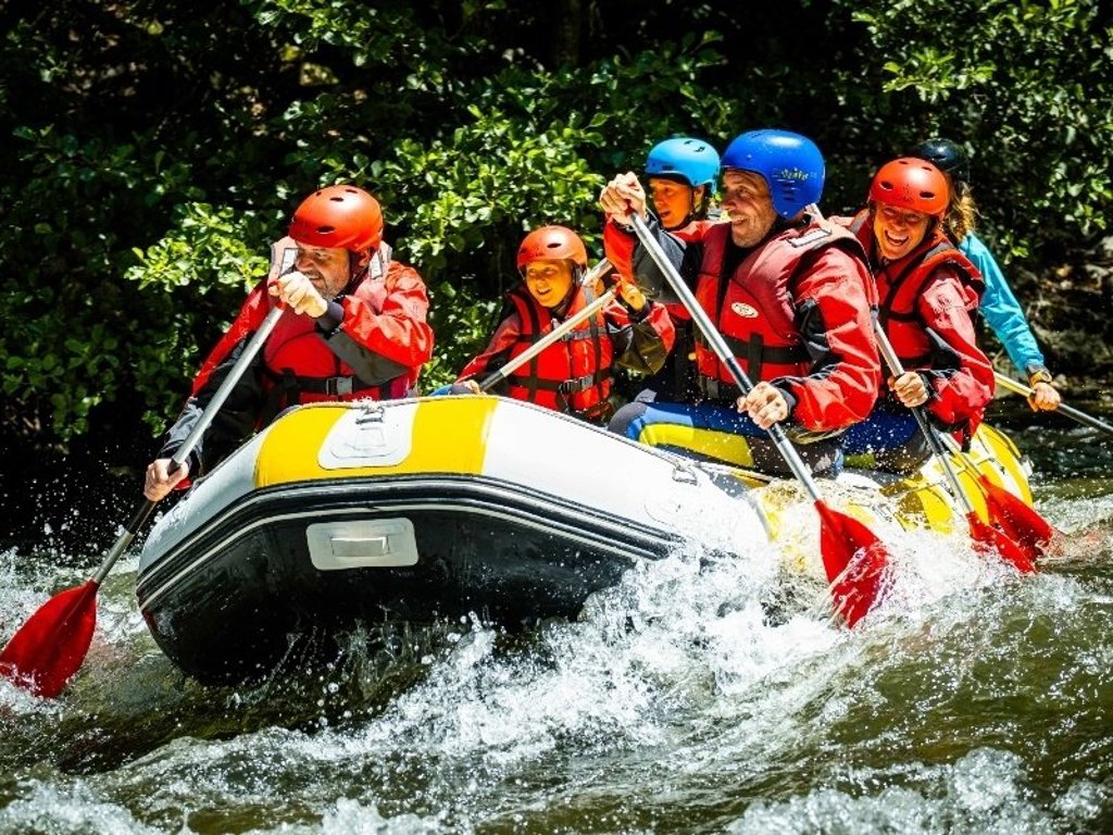 Gezin in wetsuits peddelt samen in een kano op een rivier in de Pyreneeën bij Canigou, Frankrijk.