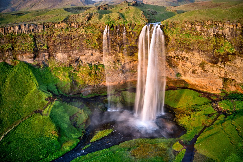Waterval Seljalandsfoss in IJsland, met groen landschap en wandelpad achter de watervallen.