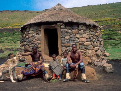 Gezin met hond voor ronde stenen hut met rieten dak in de bergen van Lesotho.