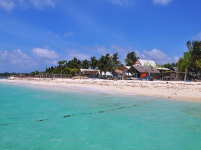 Tropisch strand met palmbomen en vissershuisjes aan helderblauw water op Sulawesi, Indonesië.