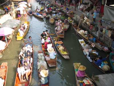 Drukke drijvende markt in Thailand met boten vol fruit, etenswaren en toeristen op een kanaal.