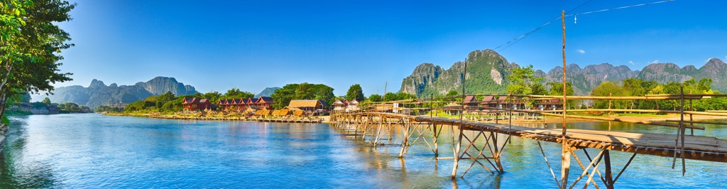 Bamboebrug over de Nam Song-rivier bij Vang Vieng, Laos, met karstbergen op de achtergrond.